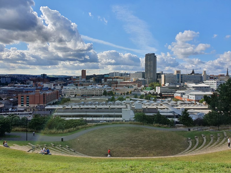 A view over the Sheffield city centre skyline on a sunny day as people relax on the grass