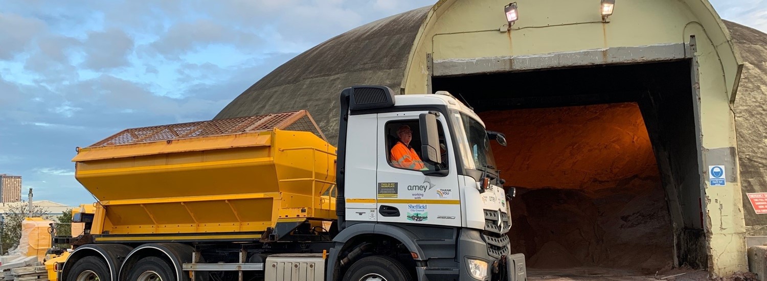 Yellow & white gritting lorry in front of concrete salt dome